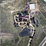 Aerial view of a rural property in Aledo, TX, with a house, trees, circular driveway, pond, and open grassy areas; bordered by 2301 FM 1187 and other fenced properties.