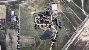 Aerial view of a rural property in Aledo, TX, with a house, trees, circular driveway, pond, and open grassy areas; bordered by 2301 FM 1187 and other fenced properties.