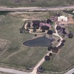 Aerial view of a rural Aledo, TX property at 2301 FM 1187 with a large house, several smaller buildings, a pond surrounded by trees, fenced areas, and adjacent roads and fields.