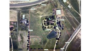 Aerial view of a fenced rural property in Aledo, TX, at 2301 FM 1187, featuring a central house, surrounding trees, pond, driveways, outbuildings, and open grassy areas. Distance measurements are marked along the fence.