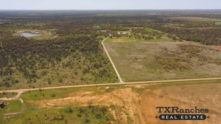 Aerial view of a rural landscape near 1502 Jones Rd, Woodson TX, with fields, sparse trees, a dirt road dividing the land, and a pond in the distance. The "TX Ranches Real Estate" logo is visible in the bottom right corner.