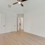 A bright, empty room with light wood flooring, white walls, a ceiling fan with lights, and three open white doors leading to other rooms or spaces.