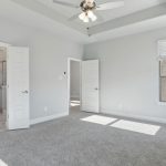 Bright, empty bedroom with light gray walls, white trim, and carpeted floor. Ceiling fan with lights is centered above. Double doors lead to a marble bathroom, and two single doors open to other rooms. Sunlight streams through windows.