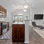 Modern open-concept kitchen and living room with dark wood cabinets, stainless steel appliances, large island, and a cozy seating area with a fireplace and wall-mounted TV.