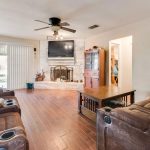 Cozy living room with brown recliners, a wooden coffee table, and a fireplace beneath a wall-mounted TV. Sliding glass doors let in natural light, and a ceiling fan hangs overhead. Hardwood floors throughout.