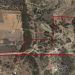 Aerial view of rural land with property boundaries outlined in red, showing roads, scattered buildings, ponds, trees, and fields within the marked area.