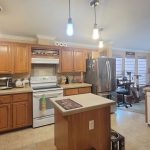 Spacious kitchen with wooden cabinets, beige countertops, an island in the center, stainless steel appliances, hanging pendant lights, and an adjacent breakfast nook with large windows.