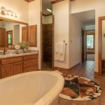 Spacious bathroom with a freestanding tub, dual-sink vanity with mirror and wood cabinets, a round animal-hide rug, open doorway to a tiled shower, and a separate toilet area. Warm wood accents throughout.