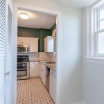 Bright kitchen with white cabinets, stainless steel appliances, tiled backsplash, and patterned tile floor. A large window lights the adjoining area, and two ceiling lights are visible.