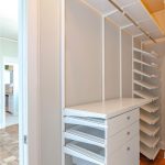A modern walk-in closet with white shelving, drawers, and hanging rods, featuring organized open shelves and mesh pull-out drawers on a wood floor.