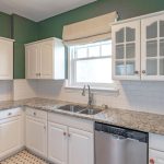 Modern kitchen with white cabinets, granite countertops, stainless steel appliances, a double sink under a window with a beige shade, and green walls above white subway tile backsplash.