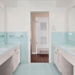 A bathroom with two sinks and vanities, blue tile countertops and backsplash, large mirrors above each sink, a white door in the center, and wooden floor visible through the open doorway.