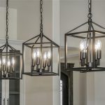 Three modern black metal pendant lights with exposed bulbs hang from the ceiling in a row, illuminating a neutral-toned room with light walls and built-in cabinetry in the background.