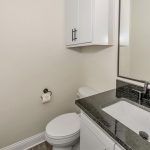 A modern bathroom with a white toilet, black countertop sink, white cabinets, large mirror, and a roll of toilet paper on the wall. The walls are light-colored and the door is white with horizontal panels.