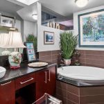 Modern bathroom with a round bathtub, vessel sink, dark wood cabinets, potted plants, decorative lamps, and framed artwork on the walls. Towels, toiletries, and artwork add a cozy, personalized touch.