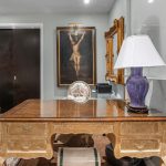 Elegant office with a vintage wooden desk, purple table lamp, ornate mirror, classic artwork, a plush sofa with cushions, and a decorative rug. The room features luxurious, traditional decor and soft lighting.