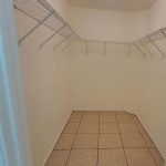 Empty walk-in closet with beige tiled floor, white walls, and wire shelving along three walls; a single ceiling light illuminates the space.
