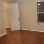 An empty room with wood flooring, beige walls, a ceiling fan with lights, an open door leading to a walk-in closet, and a window with closed blinds.