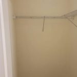 Empty walk-in closet with cream-colored walls, a single ceiling light, dark wood floor, and a white wire shelf running along two walls.