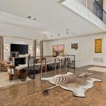 Spacious living room with high ceilings, large windows, a fireplace, modern furnishings, animal decor, and a zebra-print rug on wooden floors. Light walls and natural light create an airy, open atmosphere.