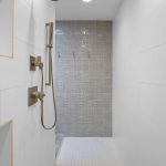 Modern walk-in shower with white tiled walls, built-in shelves, a silver rainfall showerhead and controls, and a textured gray accent wall at the far end.