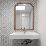 A rectangular white wall-mounted sink beneath a large wooden-framed mirror, set against a patterned tile accent wall in a minimalist bathroom.