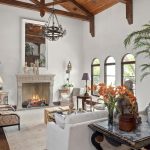 Elegant living room with vaulted wooden ceiling, exposed beams, and chandelier. Features a fireplace, comfortable seating, large potted plant, arched windows, and eclectic décor, creating a warm, inviting atmosphere.