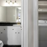 View through two doorways shows a bathroom with a sink, mirror, and toilet on the left, and a laundry room with a washer, dryer, and shelves on the right.