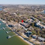 Aerial view of lakeside homes surrounded by trees, with docks extending into the water. A red location pin highlights a specific house near the shoreline.