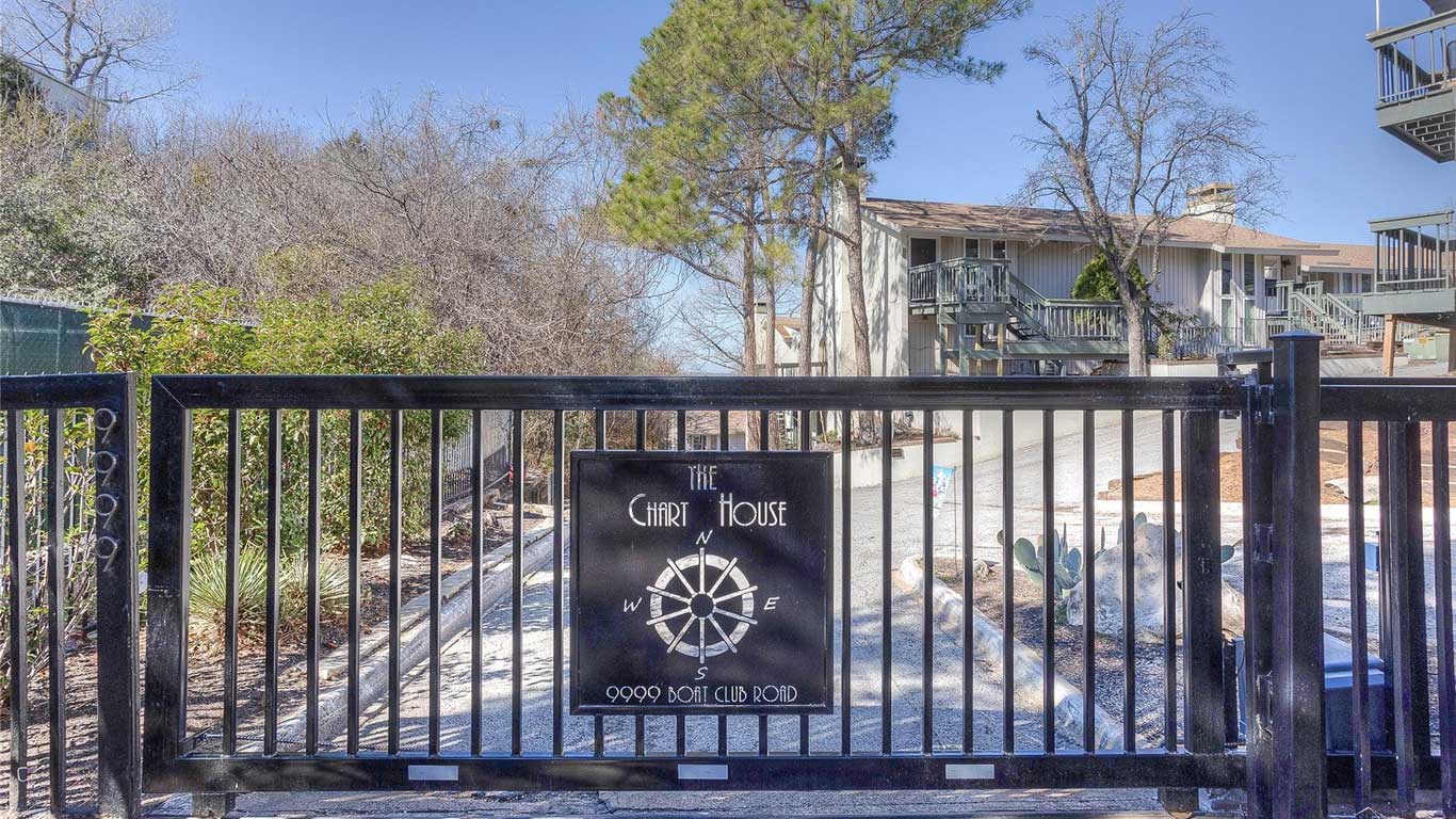 A black metal gate with a sign reading "The Chart House, 9999 Boat Club Road" blocks the entrance to a driveway, with apartment buildings and trees visible in the background.