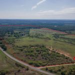 Aerial view of a large, open, grassy property bordered by a road on one side and outlined in red, with scattered trees and brush; a "Gate" pin marks an entrance near the roadside.