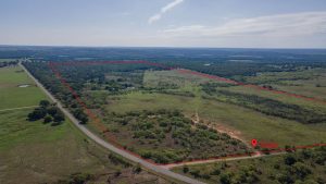 Aerial view of a large, open, grassy property bordered by a road on one side and outlined in red, with scattered trees and brush; a "Gate" pin marks an entrance near the roadside.