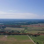 Aerial view of a large rural landscape showing fields, trees, and ponds under a clear blue sky, with a rectangular area outlined in red.