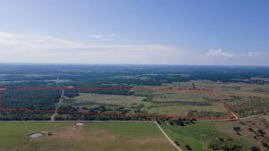 Aerial view of a large rural landscape showing fields, trees, and ponds under a clear blue sky, with a rectangular area outlined in red.