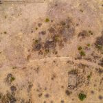 Aerial view of a dry, sparsely vegetated landscape at Historic S&S Ranch, with scattered small green bushes, faint paths, and rectangular outlines suggesting old structures or foundations.