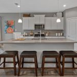 Modern kitchen with white cabinets, stainless steel appliances, a large island with four dark wooden stools, and a dining area with a round table set for breakfast near bright windows.