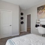 A modern bedroom with a bed, a window with curtains, a white door, a wall-mounted desk with a chair, decorative purple wall accents, and geometric wall art above the desk.