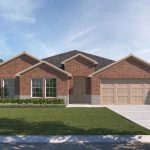 Single-story brick house with tan trim and a double garage, set on a manicured lawn with shrubs and trees. A wide driveway leads to the garage, and the sky is clear with a few clouds.
