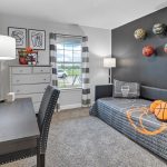 A modern bedroom with a gray daybed, basketball-themed pillows, and basketballs mounted on a dark accent wall. A desk, dresser, and window with striped curtains complete the cozy, sporty decor.