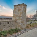 A stone monument sign reading "The Parks of Alvarado" stands at the entrance of a residential neighborhood, with a house, landscaping, and a sunset sky in the background.