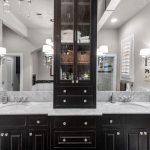 Elegant bathroom with double sinks, dark wood cabinets, marble countertop, a mirrored cabinet in the center, wall-mounted lights, and decorative “Mr.” and “Mrs.” signs on either side of the sinks.