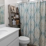 A small bathroom with a white vanity and sink, silver faucet, toilet, blue and white patterned shower curtain, and a wooden ladder shelf holding decor, baskets, and toiletries.