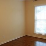 An empty room with light beige walls, two large windows with white blinds, a white baseboard, and dark wood flooring. Natural light enters through the windows, brightening the space.