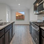 Modern kitchen with dark wood cabinets, granite countertops, stainless steel appliances, a dual sink on an island, a gas stove, microwave, and light wood flooring. Large window and outside view in the background.