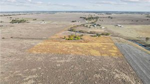 Aerial view of a large, dry farmland with a rectangular section highlighted. The highlighted area contains a small pond surrounded by trees, while the surrounding land appears mostly barren. Scattered farms and fields are visible in the distance.