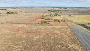 Aerial view of a rural landscape with fields and scattered houses; a red outline marks the boundary of a specific plot of land in the center of the image.